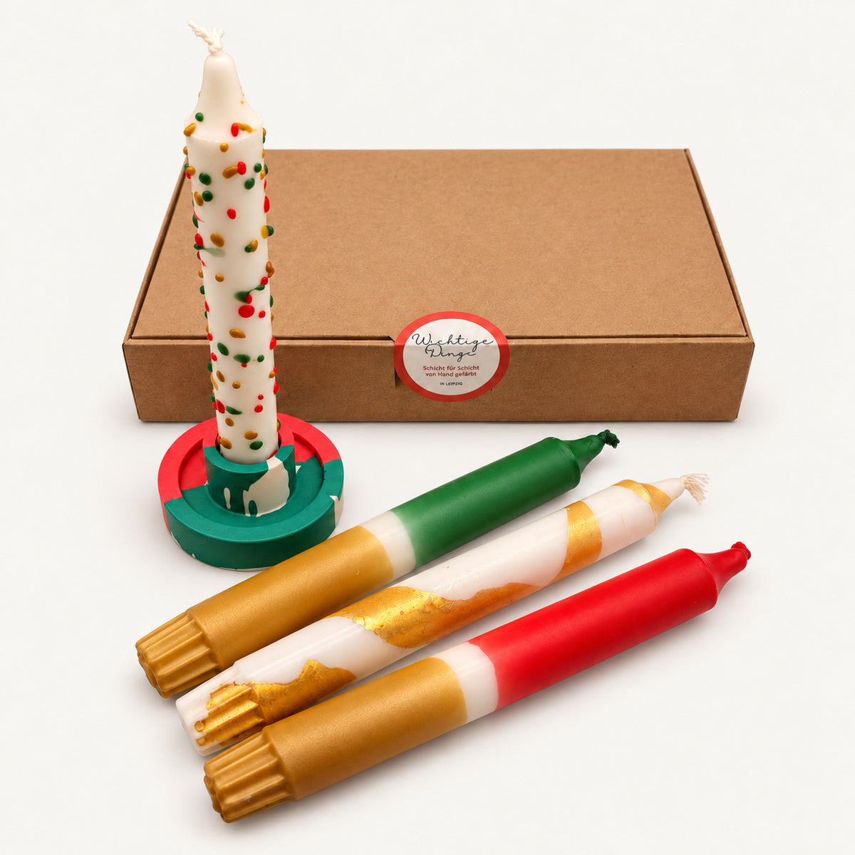 Geschenkset Weihnachtstisch: vier Dip-Dye-Stabkerzen in Rot, Grün und Gold mit Kerzenständer vor der Geschenkbox