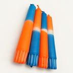Neon Blue Flame – vier handgefärbte Stabkerzen in Neonorange und Blau auf neutralem warmweißem Hintergrund, schräge Detailansicht