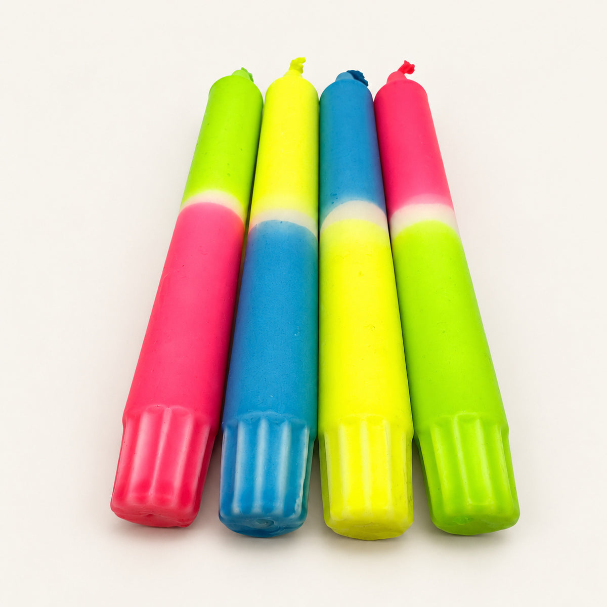 Rainbow Candyshop – vier handgefärbte Neon-Stabkerzen in Grün, Blau, Pink und Gelb auf neutralem warmweißem Hintergrund, Blick vom Kerzenfuß