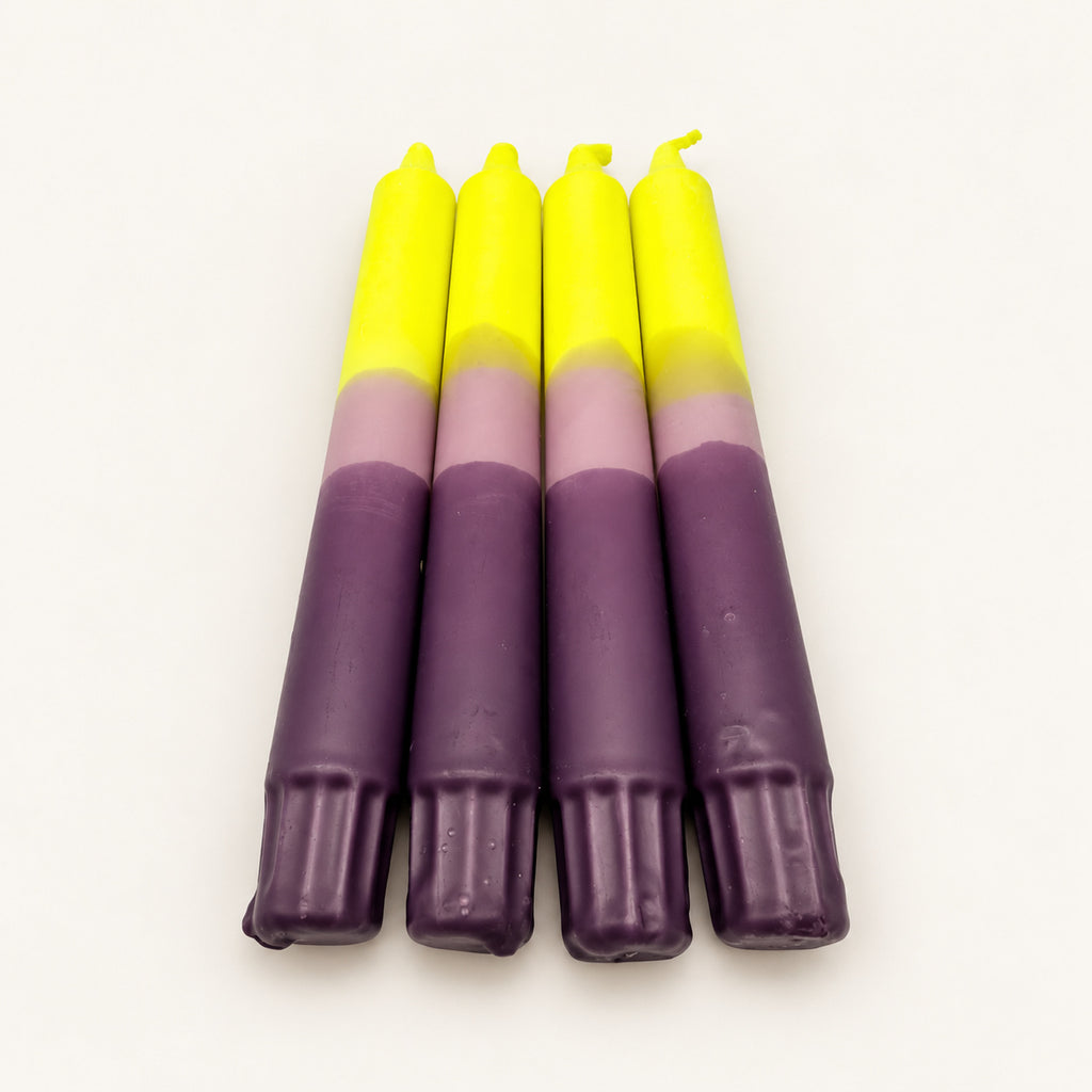 Sunset Lavender – vier Dip Dye Stabkerzen in Neongelb, Flieder und Lila auf neutralem warmweißem Hintergrund, Blick vom Kerzenfuß