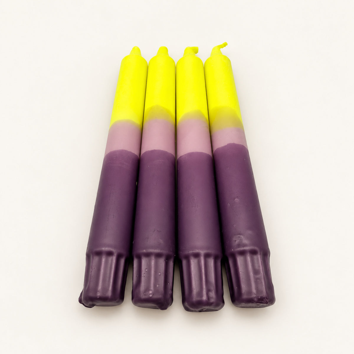 Sunset Lavender – vier Dip Dye Stabkerzen in Neongelb, Flieder und Lila auf neutralem warmweißem Hintergrund, Blick vom Kerzenfuß